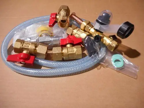 Zusammenstellung von Messingventilen, Absperrhähnen und Kunststoffschläuchen, die Teil eines Hahn Sets von Remeha sind, auf braunem Untergrund aus Karton.